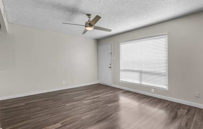 the spacious living room with a large window and a ceiling fan