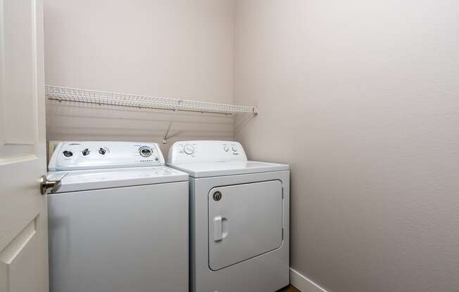 a washer and dryer in the corner of a room with a shelf above