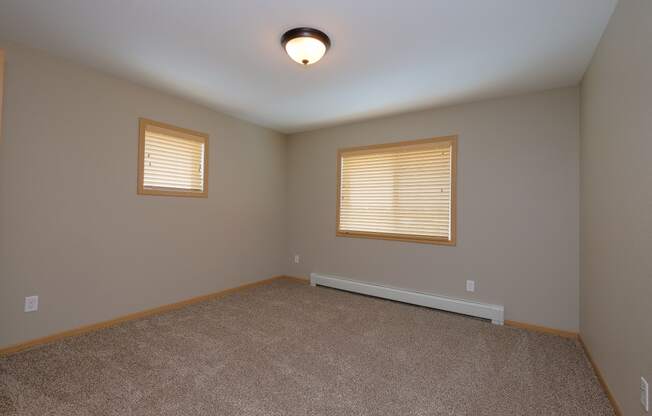 a bedroom with two windows and a carpet. Fargo, ND Urban Plains Apartments