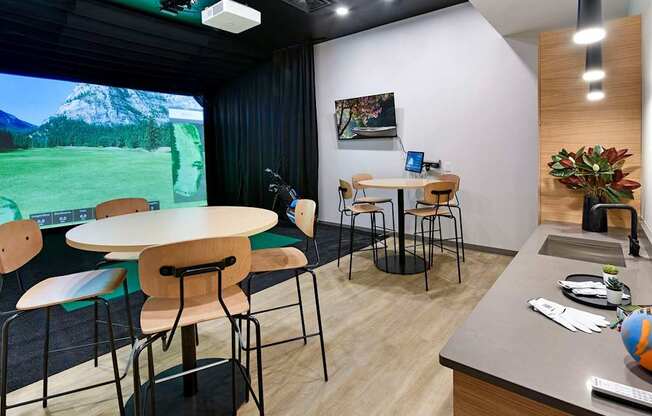 A room with a table, chairs, and a large screen displaying a mountainous landscape.