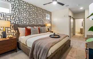 A bedroom with a patterned wallpaper and a bed with a grey blanket.