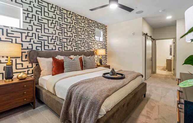 A bedroom with a patterned wallpaper and a bed with a grey blanket.