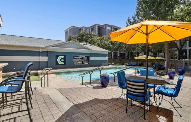 A pool area with chairs and a yellow umbrella at Encore at Buckingham Apartments in Richardson, TX