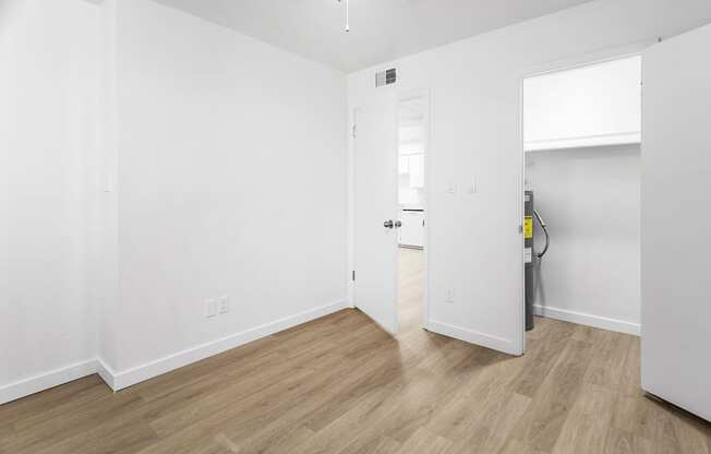 a bedroom with white walls and wood flooring and a door to a bathroom