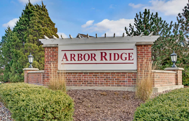 A welcoming community monument sign here at Arbor Ridge featuring classic brick pillars, elegant lantern lights, and landscaped greenery. The clean white lettering and charming pergola detail create a warm, inviting entrance.