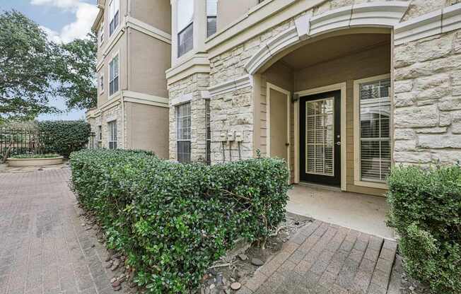 A building with a black door and window is surrounded by green bushes.