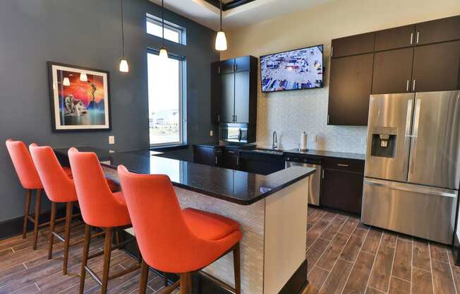 a kitchen with a bar with orange chairs and a stainless steel refrigerator