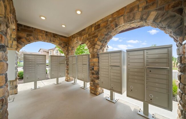 A row of mailboxes are lined up on a sidewalk under a stone archway.