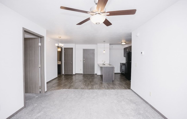 an empty living room with a ceiling fan and a kitchen