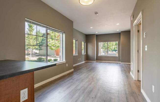 A large empty room with wooden floors and a window overlooking a tree-filled street.