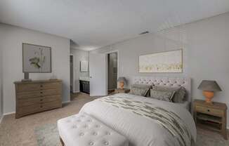 A bedroom with a large bed, a dresser, and a nightstand with a lamp.