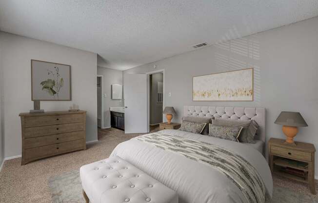 A bedroom with a large bed, a dresser, and a nightstand with a lamp.