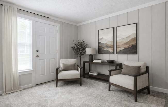 A living room with a white door, two chairs, a table, and two pictures on the wall.