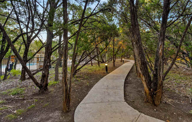 A concrete walkway leads through a grove of trees. at Bridge at Heritage Woods, Texas
