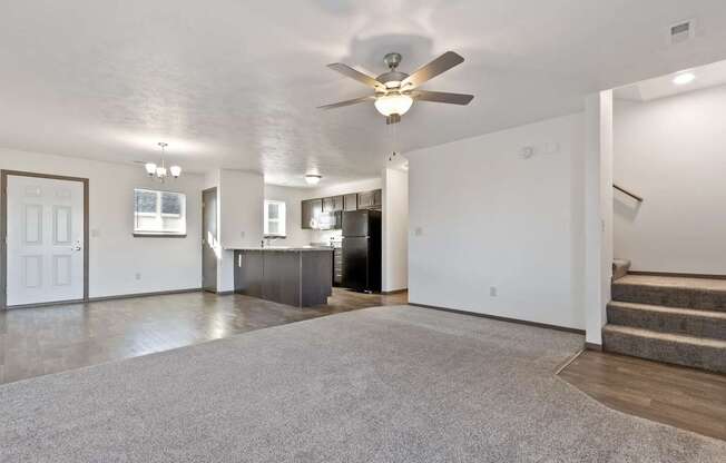 A spacious living room with a grey carpet and a ceiling fan.