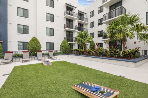 Courtyard area with cornhole boards in green space and chairs at Bay Village 1 in Palmetto Bay, FL