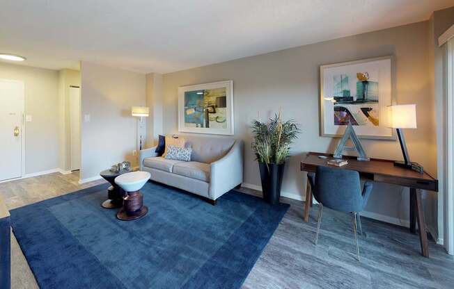 A modern living room with a white sofa, a grey armchair, a wooden desk, and a blue rug.