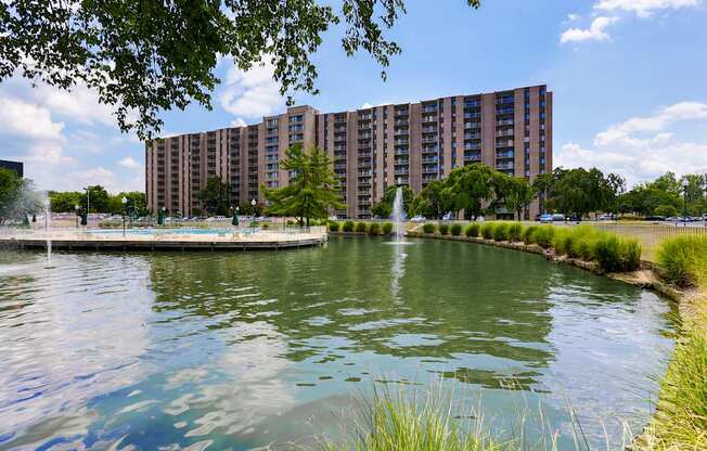 A large building is situated next to a body of water with a fountain in the middle.