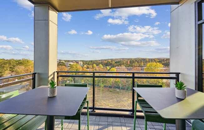 a balcony with tables and chairs and a view of a forest at Link Apartments® Calyx, Chapel Hill, 27517