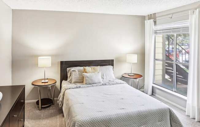 Model apartment second bedroom with a bed, two night stands with lamps, and a window at Hunters Chase Apartments in Austin, TX