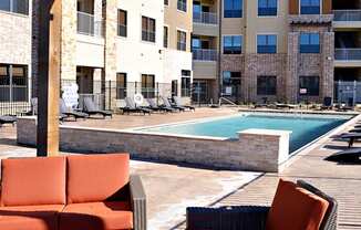 an outdoor lounge area with chairs and a pool at an apartment complex