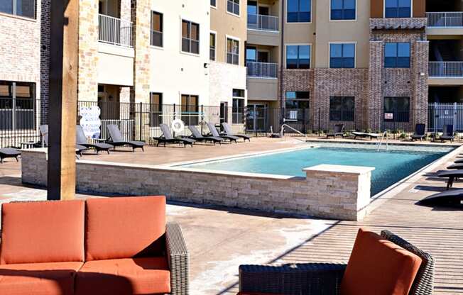 an outdoor lounge area with chairs and a pool at an apartment complex