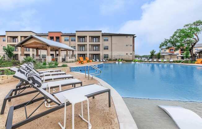 A pool area with sun loungers and a building in the background.