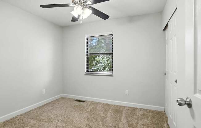 A room with a ceiling fan and a window with blinds.