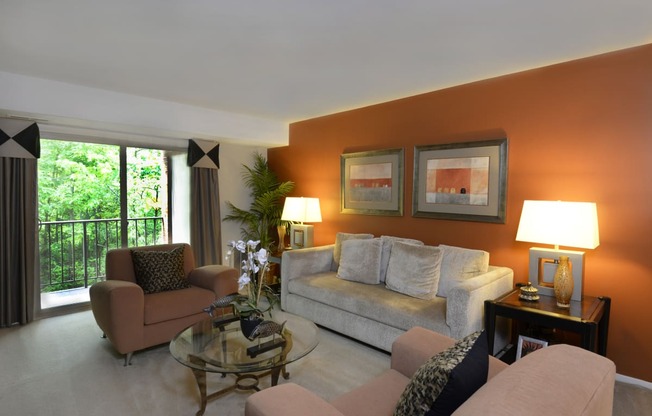 a living room with an orange accent wall and a gray couch at Liberty Gardens Apartments, Baltimore, MD 21244