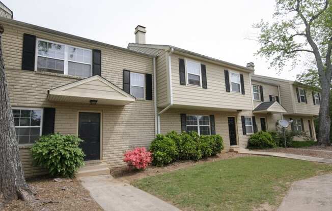 the front of a tan house with black shutters and a lawn and a sidewalk