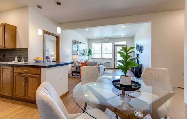 a dining area with a glass table and chairs and a kitchen in the background
