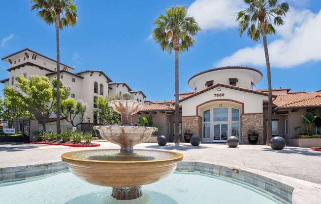 A fountain in front of a building with palm trees in the background.