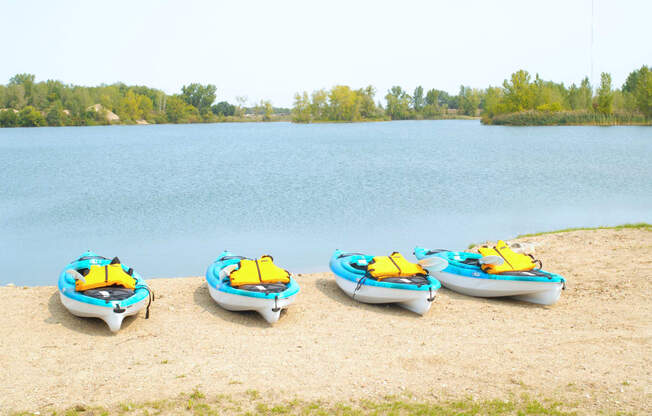 Lake with sand beach. On the beach there are four kayaks. All of the kayaks are blue with yellow life vests on them.