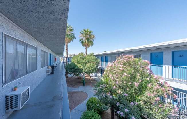 Balcony view of a courtyard with a sidewalk and trees between two apartment buildings.