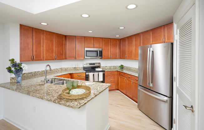 This stylish kitchen serves both the main living space and the adjacent den, featuring upgraded stainless steel appliances and modern lighting. The existing custom cabinetry and granite countertops are complemented by the rich tones of new vinyl plank wood-style flooring.