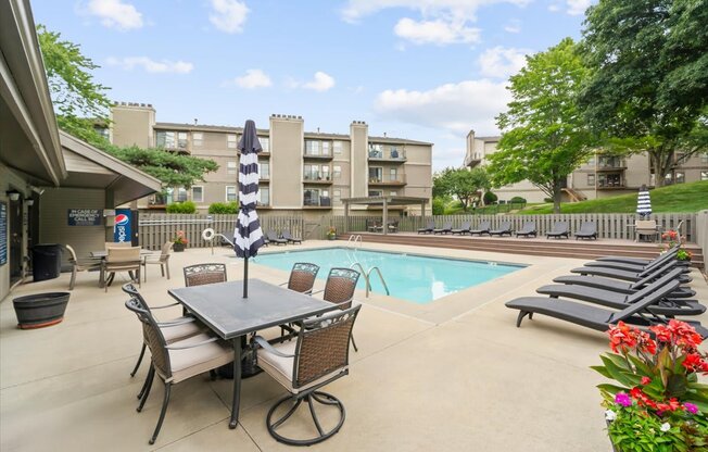 A pool area with a table and chairs and a striped umbrella.
