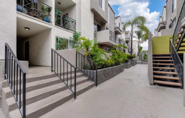Community grounds and walk path throughout the property.  Several planters with greenery and palm trees.  There are staircases that lead up to the 2nd floor homes along the walkway. 