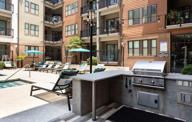 an outdoor kitchen with a grill and lounge chairs in front of an apartment building