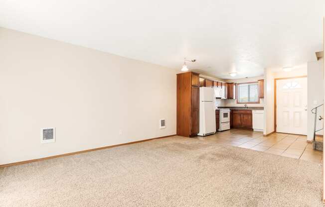 a living room with beige carpet and a kitchen in the background