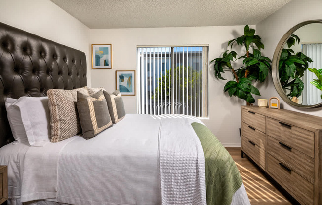 A bedroom with a large bed, a mirror, and a plant.