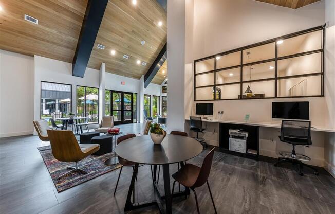 A clubhouse with four seating areas and a built-in office area with two chairs, a printer, and two computers near doors leading to a community pool.