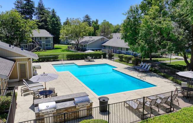 a swimming pool with lounge chairs and umbrellas in front of a house