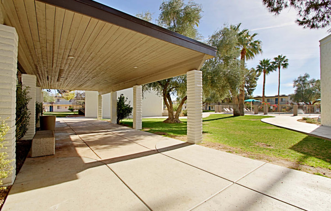 a covered walkway with trees and a building in the background