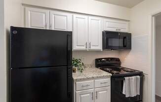 A kitchen with black appliances and white cabinets in a 2 bedroom, 2 bath 970 square foot apartment home at Preston Park Apartments in the Far North Dallas neighborhood of Dallas, TX