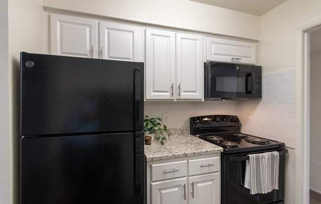 A kitchen with black appliances and white cabinets in a 2 bedroom, 2 bath 970 square foot apartment home at Preston Park Apartments in the Far North Dallas neighborhood of Dallas, TX