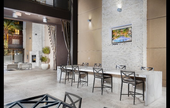 An open-air loggia with an 8-person marble dining table, seating areas, and an HDTV mounted on a stone masonry wall.