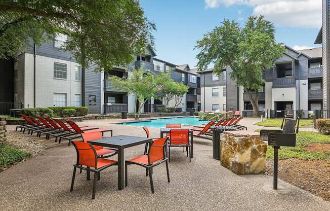 A pool surrounded by chairs and trees in front of apartment buildings.