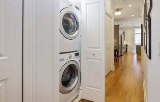 A white door is open to a hallway with a washer and dryer stacked on top of each other.