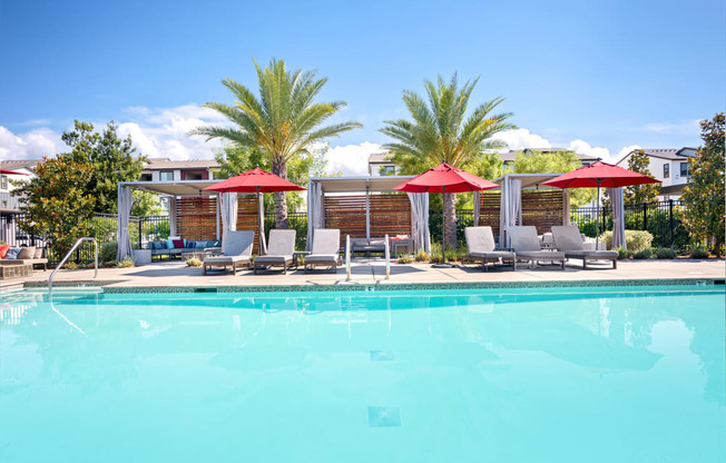 A swimming pool with red umbrellas and lounge chairs.