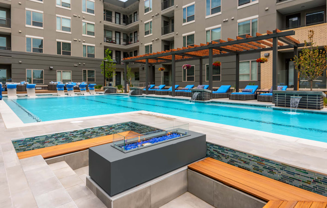 a swimming pool with a firepit and lounge chairs next to an apartment building
